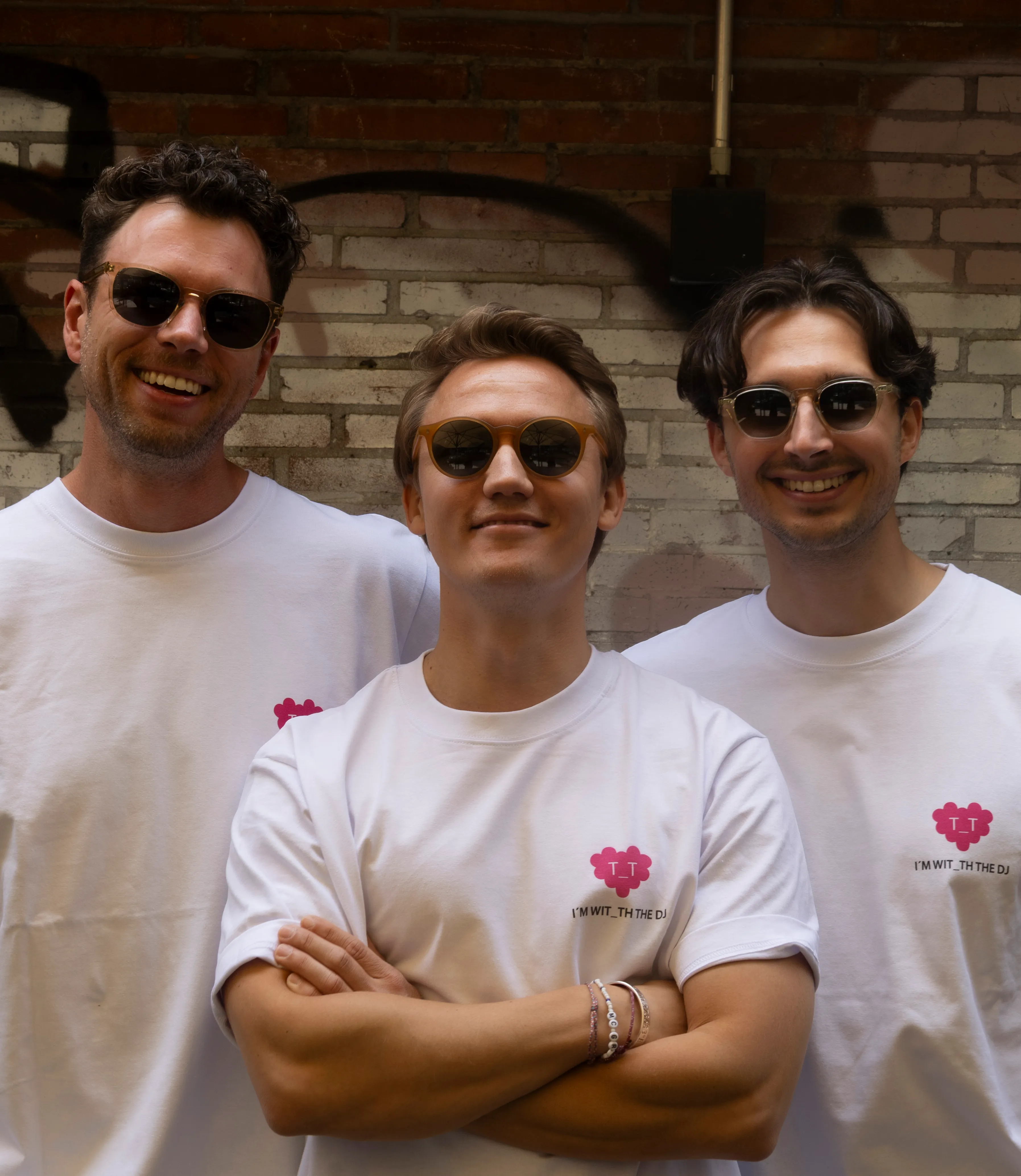 Hans, Lukas and Magnus of T_T in front of a brick wall, wearing the pink T_T shirts